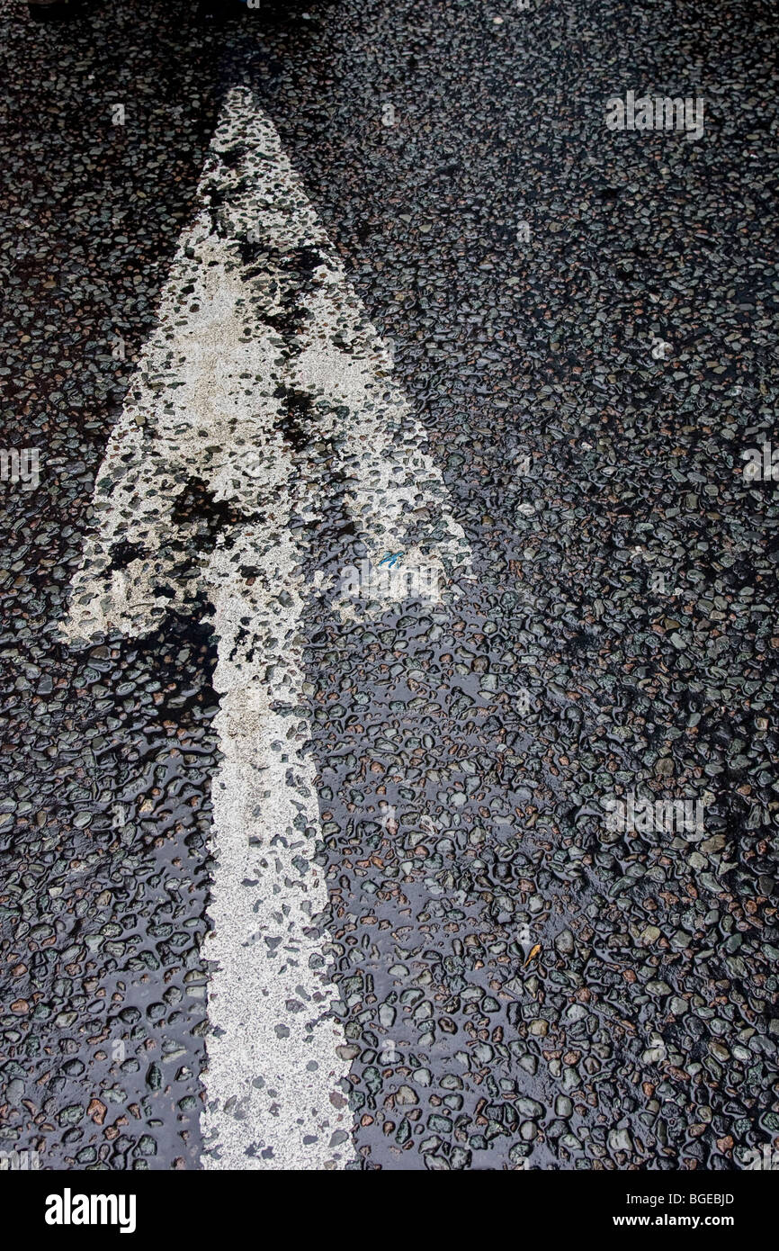 Ein Bild eines Pfeils lackiert in weiß auf nassem Asphalt. Stockfoto
