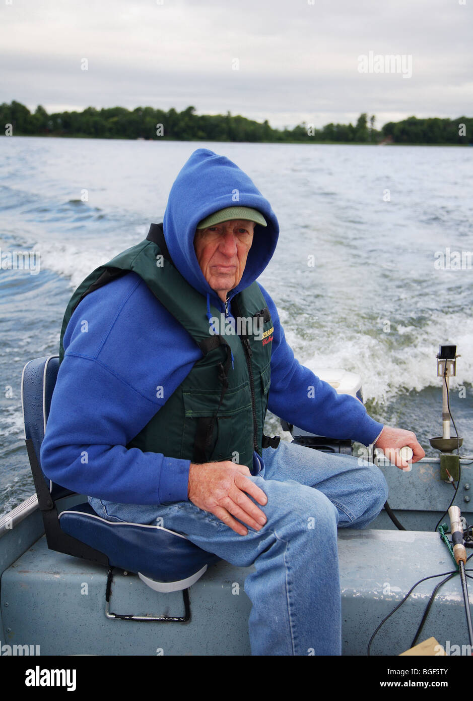 Senior ältere erfahrene Angelführer fahren Alumnacraft Fischerboot im nasskalten Wetters kabbeliges Wasser Gefolge Wellen Aktion Stockfoto