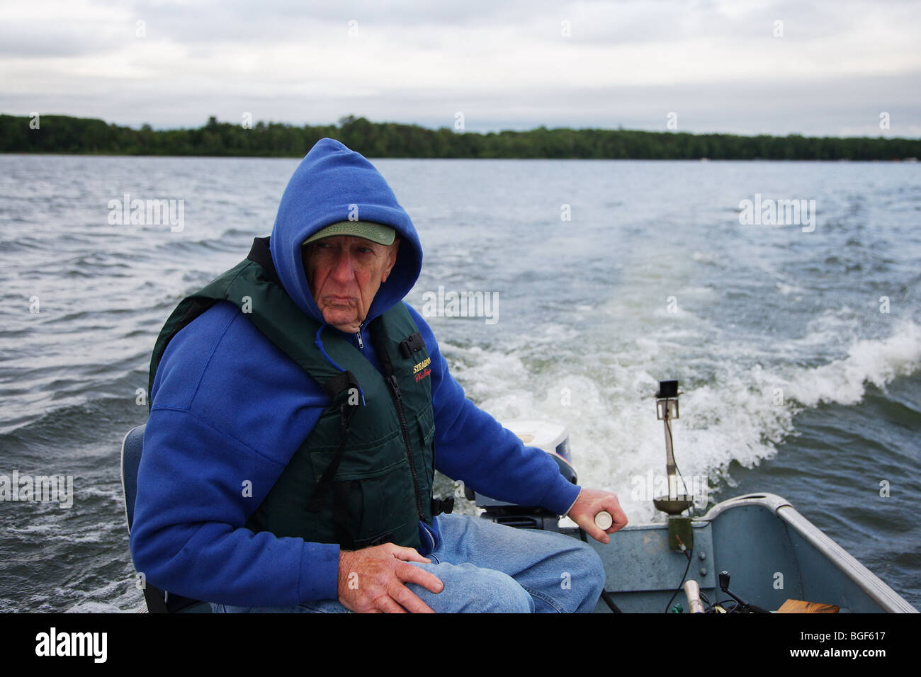 Senior ältere erfahrene Angelführer fahren Alumnacraft Fischerboot im nasskalten Wetters kabbeliges Wasser Gefolge Wellen Aktion Stockfoto