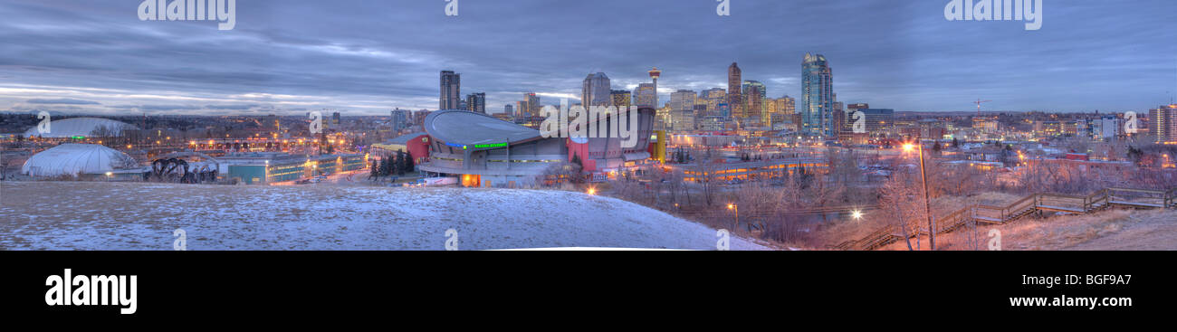 er Saddledome mit Hochhäusern und dem Calgary Tower im Hintergrund in der Dämmerung nach leichtem Schneefall im frühen Winter, Stockfoto