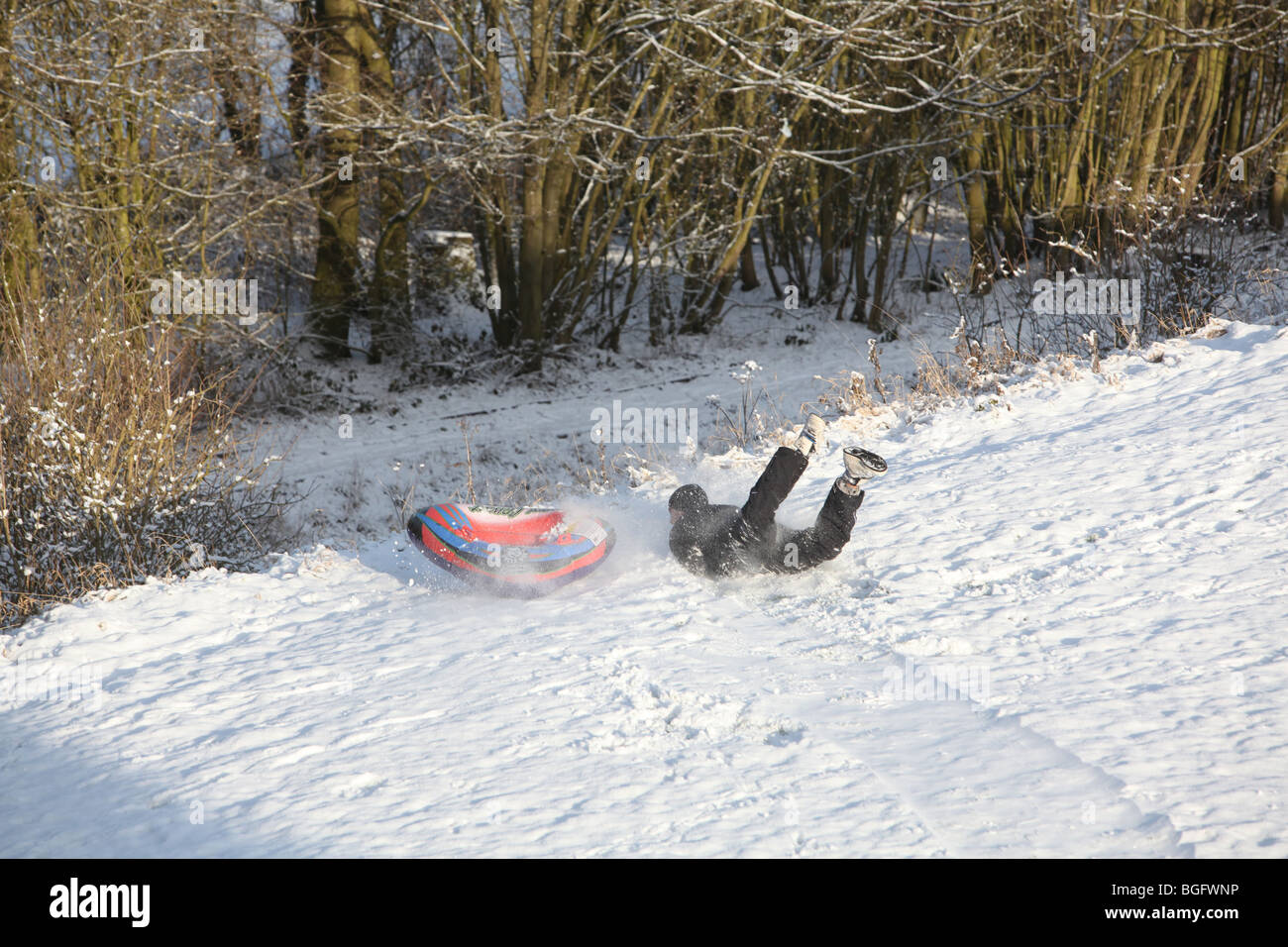 Ein Mann fällt vom eine aufblasbare Schlitten im Schnee am Rande einer steilen Abfall in der erste Schnee des Jahres 2010 Stockfoto