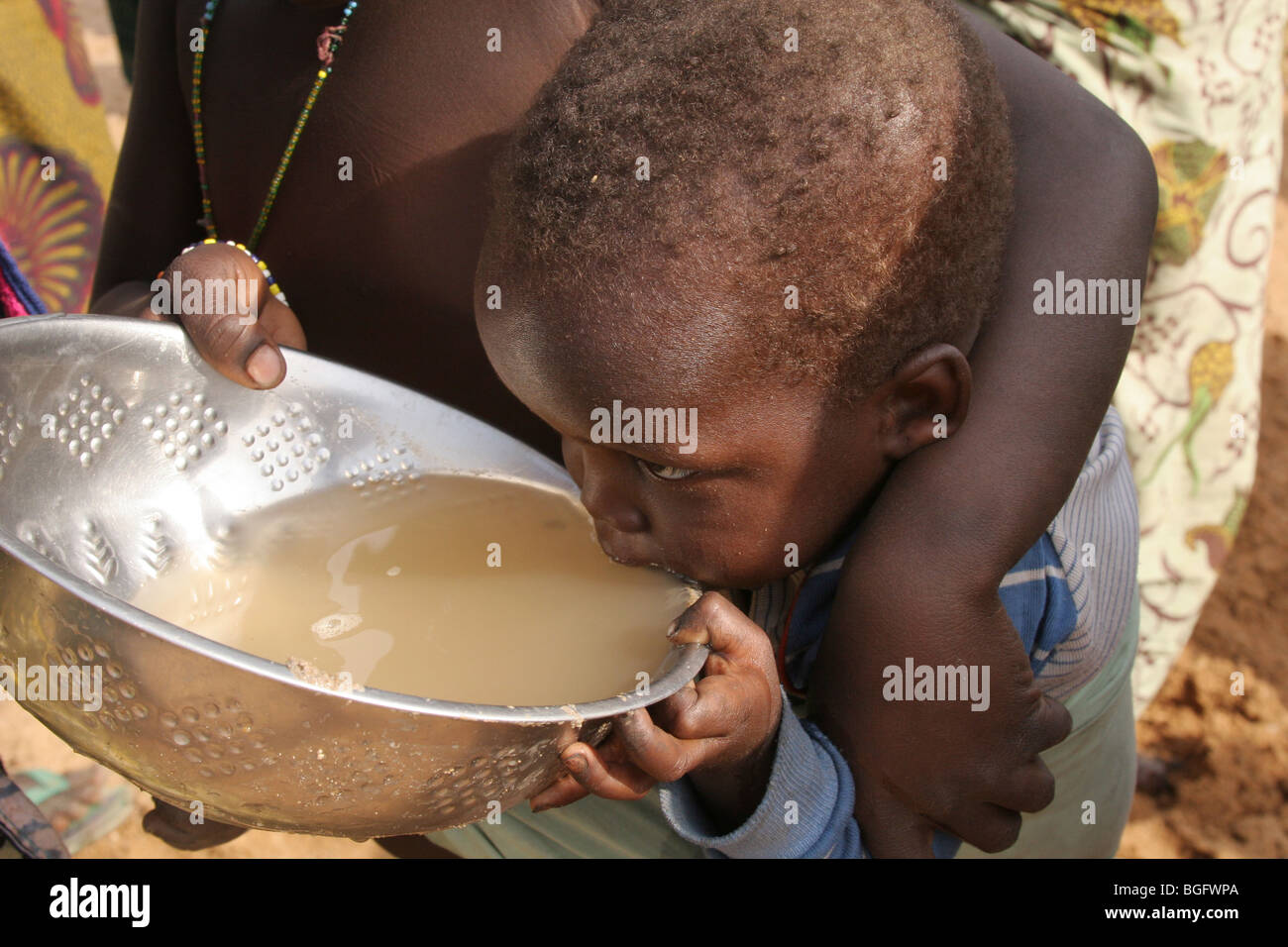 Ein junges Kind trinkt schmutziges Wasser aus einem trockenen Flussbett in Burkina Faso, Westafrika Stockfoto