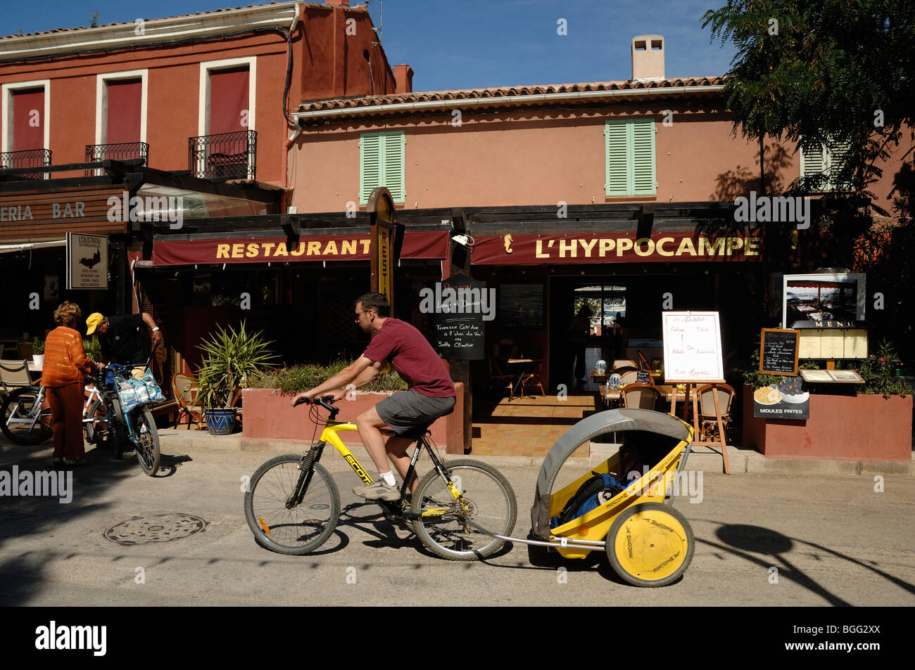 Radfahrer mit Kind Trailer Zyklen Vergangenheit Restaurants auf der Insel Porquerolles, Îles Hyères, Var, Côte d ' Azur französische Riviera Frankreich Stockfoto