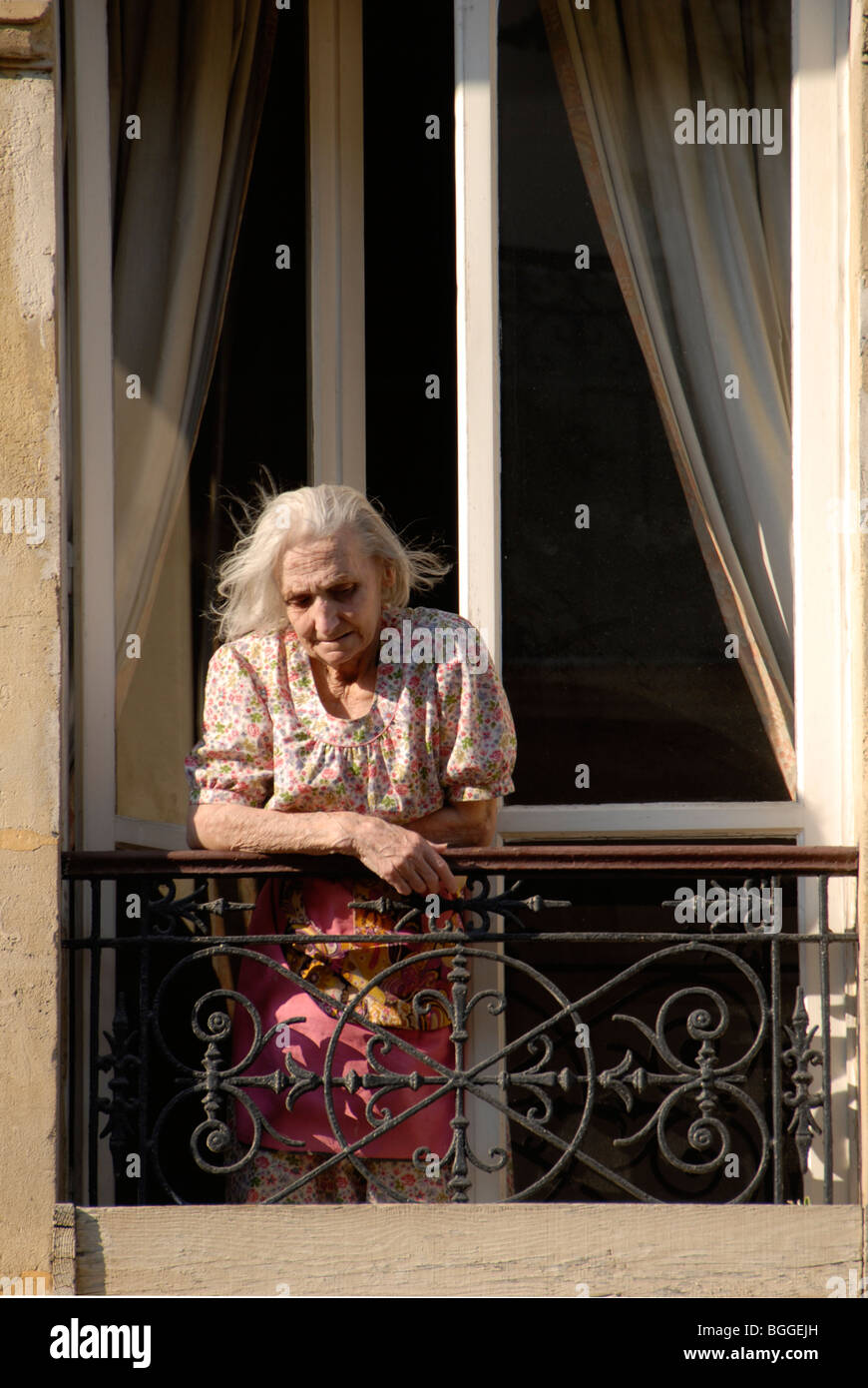 Ältere französische Frau blickt aus ihrem Balkonfenster auf die Straße unten Stockfoto