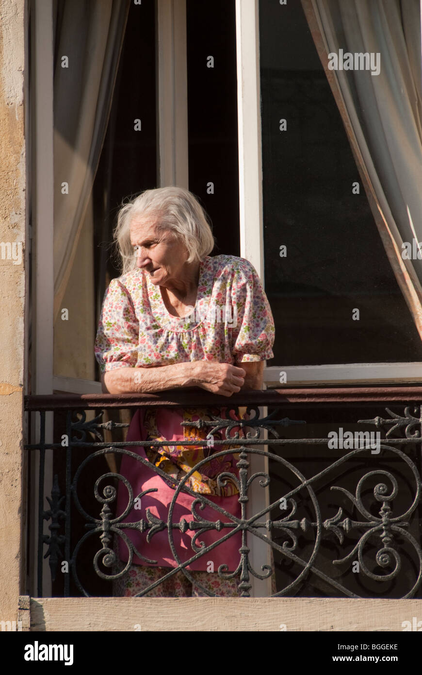 Ältere französische Frau blickt aus ihrem Balkonfenster auf die Straße unten Stockfoto