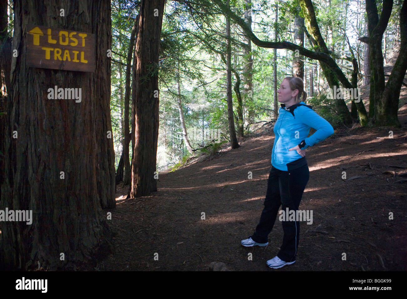 Eine Frau auf einem Trail wandern hält ein Schild zu lesen, die "Lost Trail", sagt an einer Spaltung im Pfad, Muir Woods National Monument Stockfoto