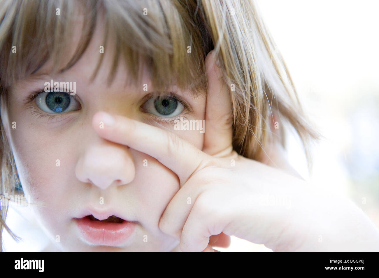 acht Jahre altes Kind, Blick in die Kamera mit den Fingern im Gesicht Stockfoto