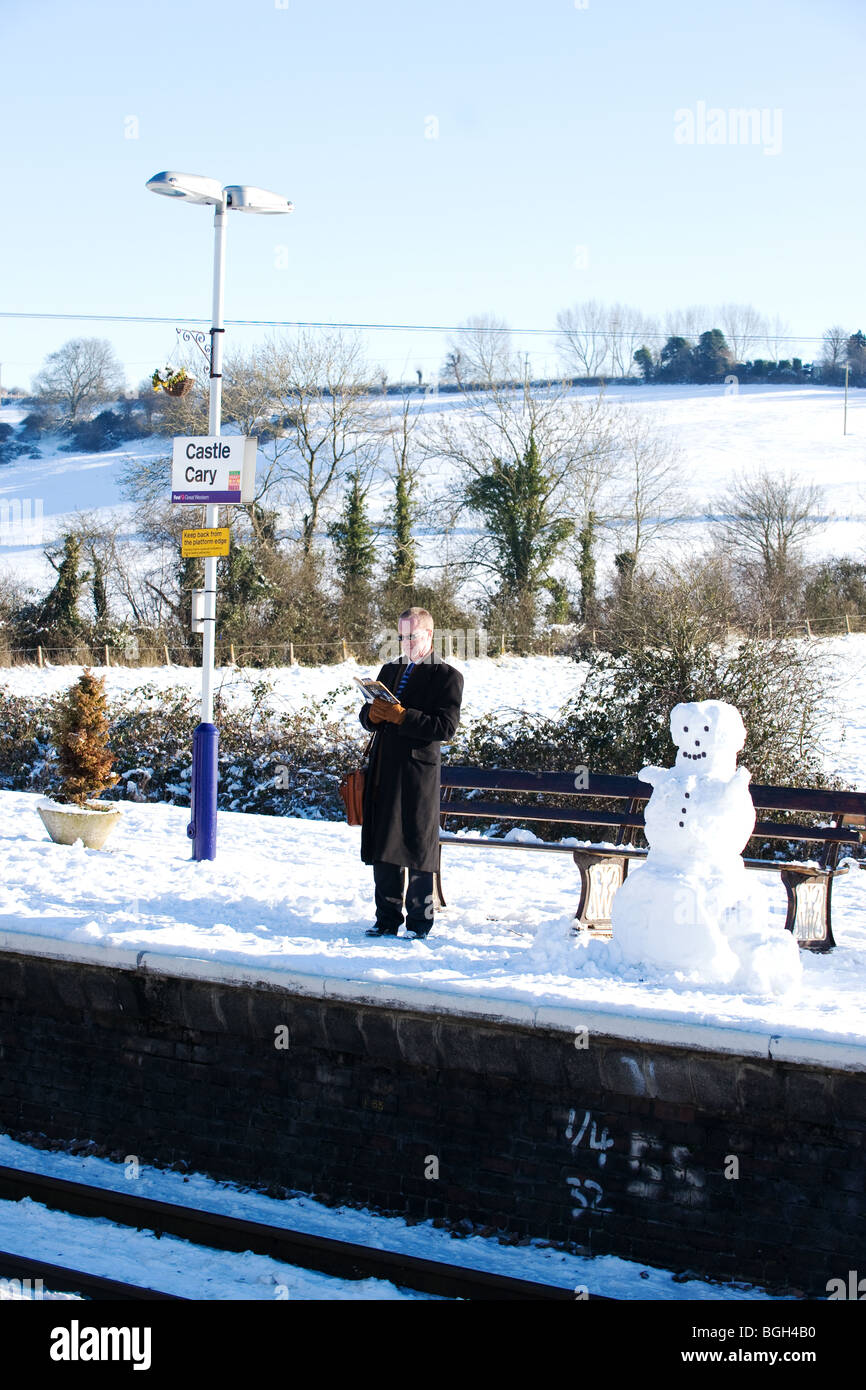 Passagier und Schneemann warten auf einen Zug im Schnee in Castle Cary Bahn Staion, Somerset, England Stockfoto