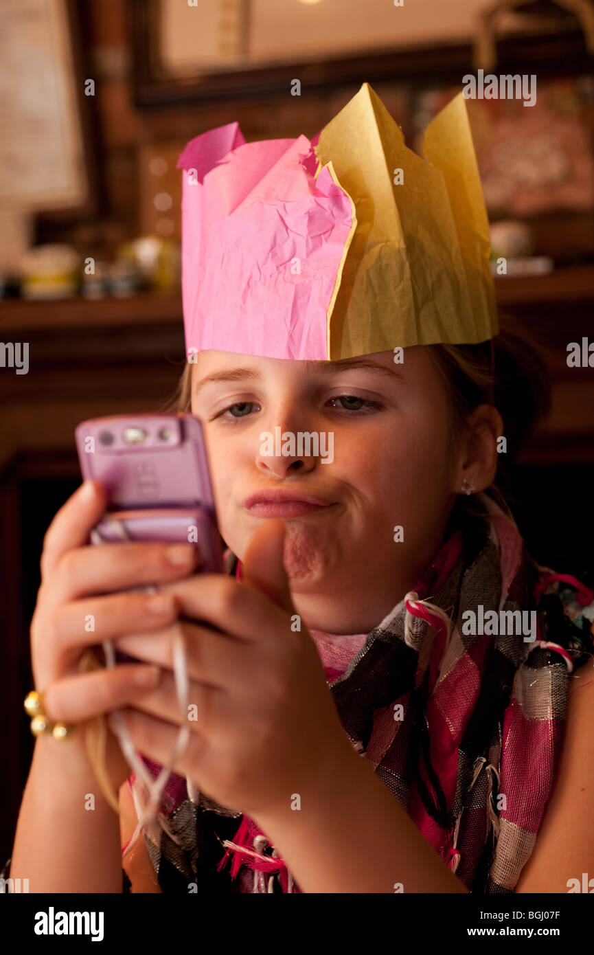 ein junge Teenager-Mädchen tragen Papier Party Hut senden oder Lesen von SMS auf ihrem Mobiltelefon nach Weihnachtsessen Stockfoto