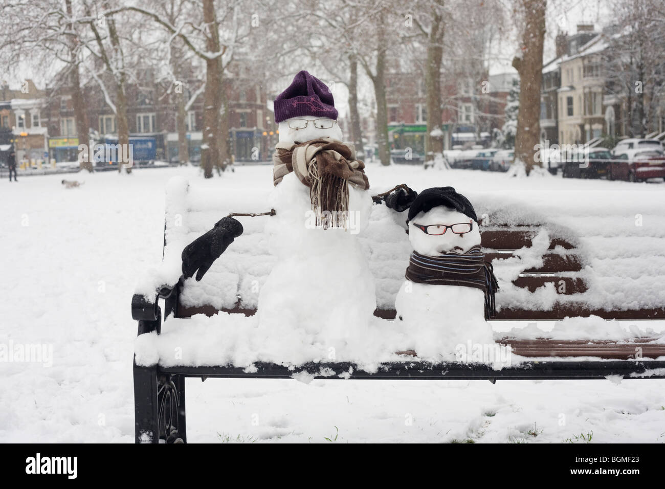 Zwei kleine Schneemänner sitzen auf einer Parkbank in Goose Green, East Dulwich, Südlondon. Stockfoto