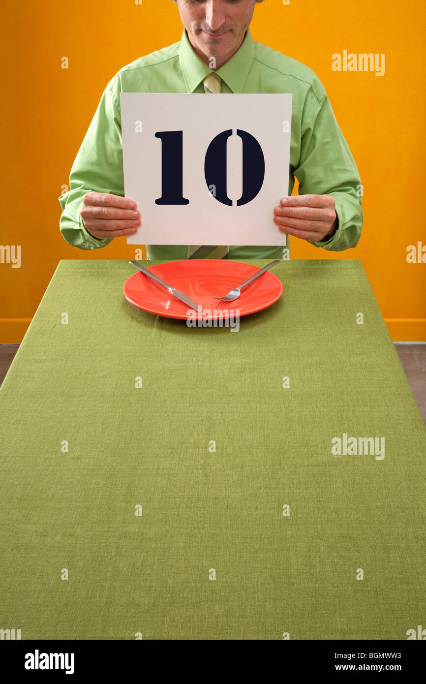 Mann am Tisch Essen hält 10 Zeichen zum Preis Essen Stockfoto