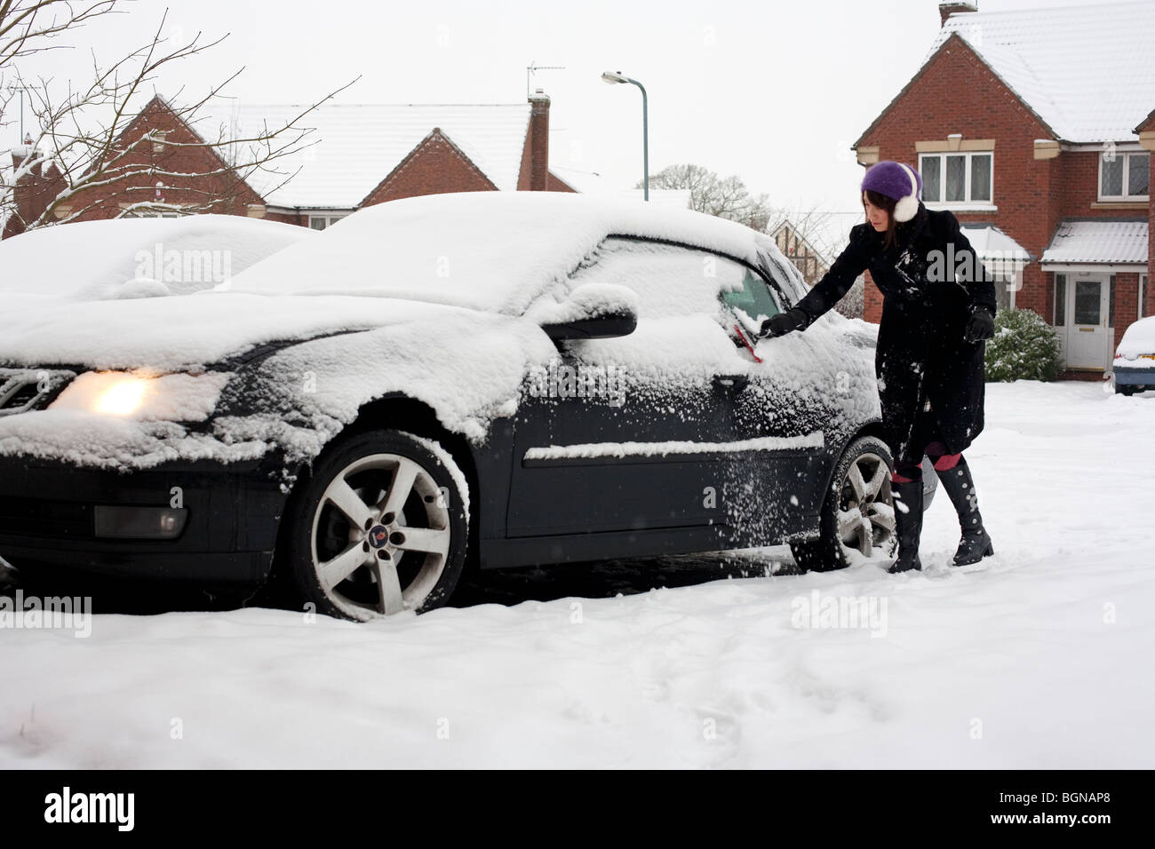 Eine Frau, die Schneeräumung von ihrem Auto auf ihrer Einfahrt in Worcestershire, UK Stockfoto