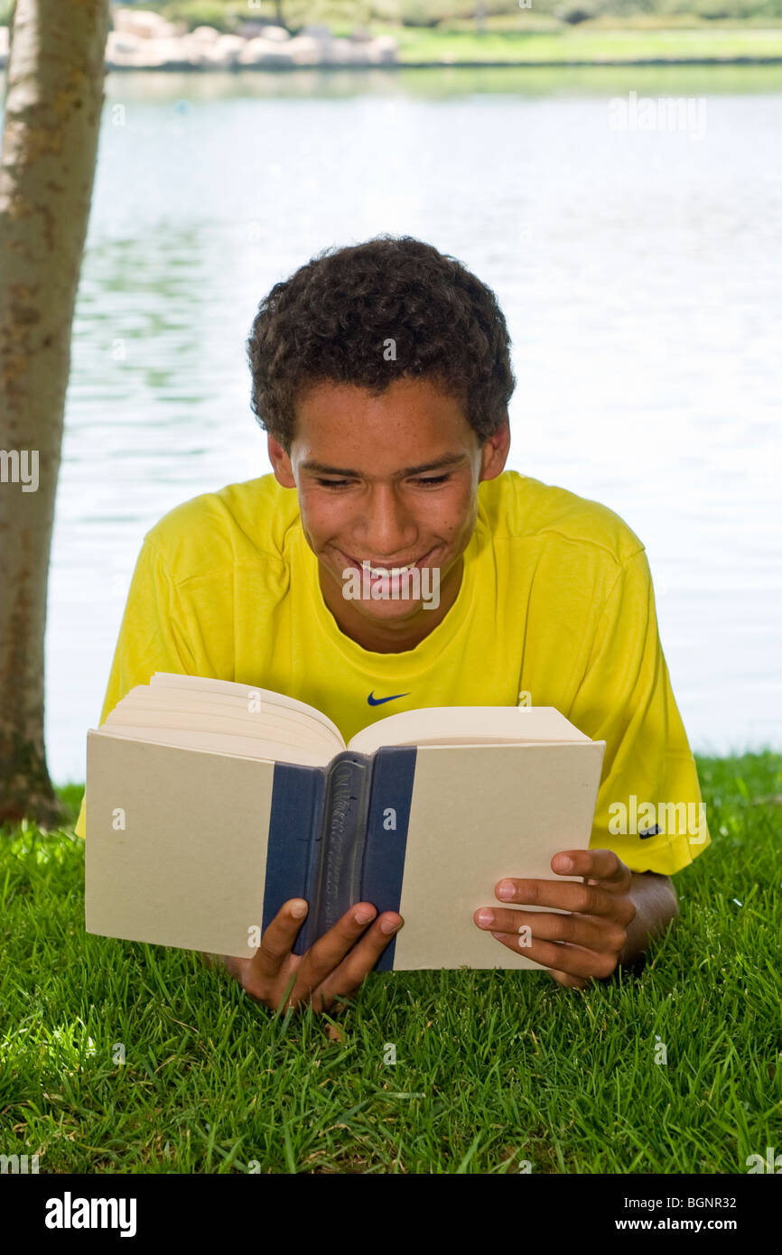 Junge Mensch Menschen 16-17 Jahre alten Jugendlichen Hispanic/African American Boy lesen im Park Schatten Baum HERR © Myrleen Pearson Stockfoto