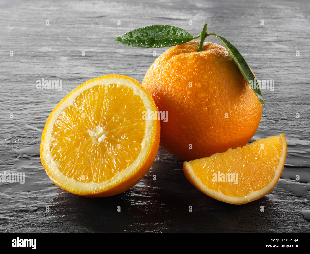 Ganze und geschnittene frische Orangen mit Blättern vor schwarzem Hintergrund Stockfoto