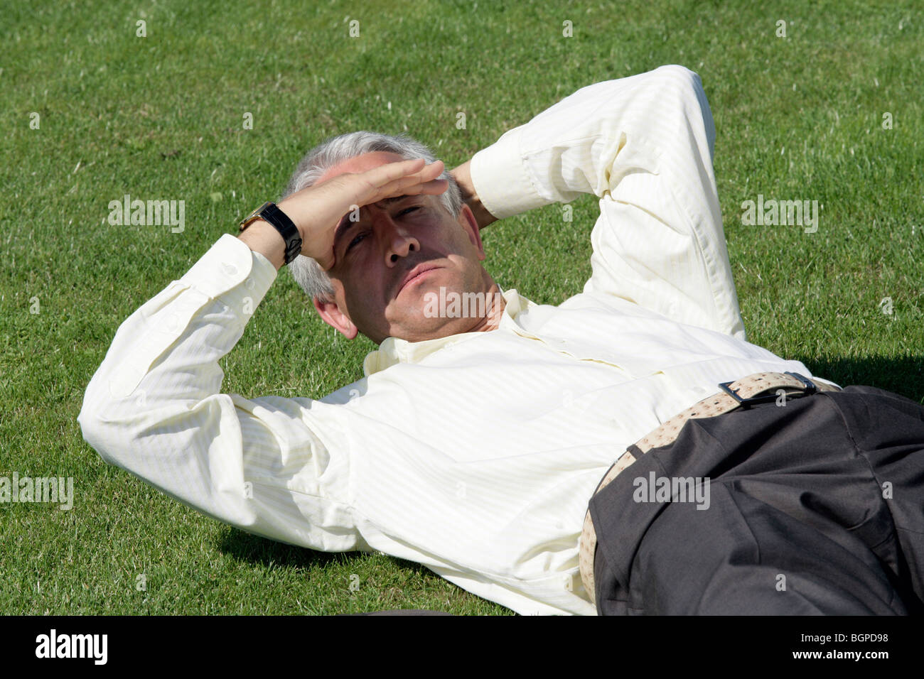 Reife niedergeschlagen Geschäftsmann liegen auf dem Rasen, die Augen vor Sonnenlicht Abschirmung Stockfoto