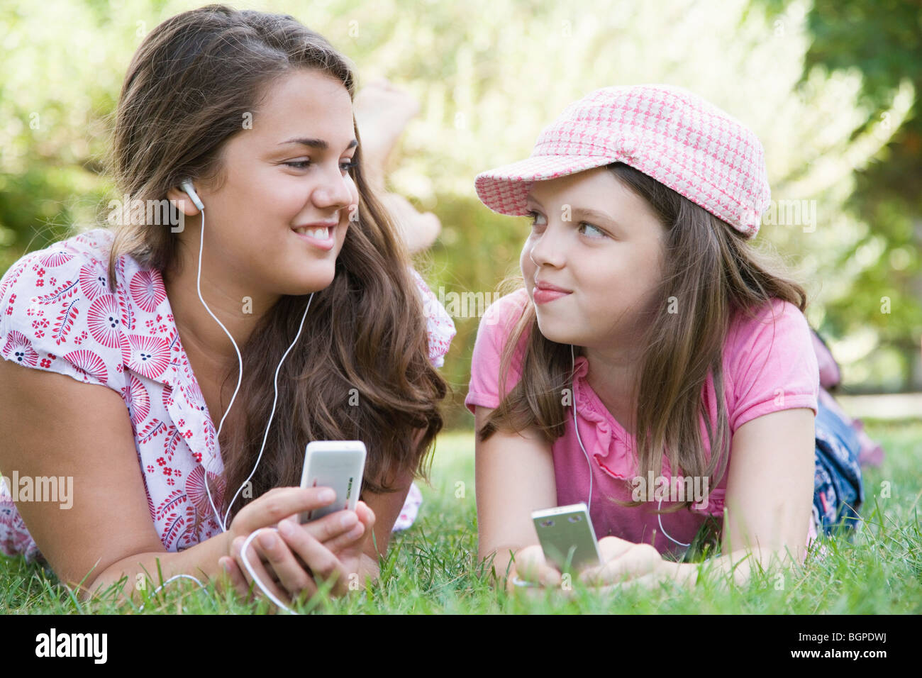 Junge Frau und ein Mädchen auf dem Rasen im Park liegen und anhören von MP3-Playern Stockfoto