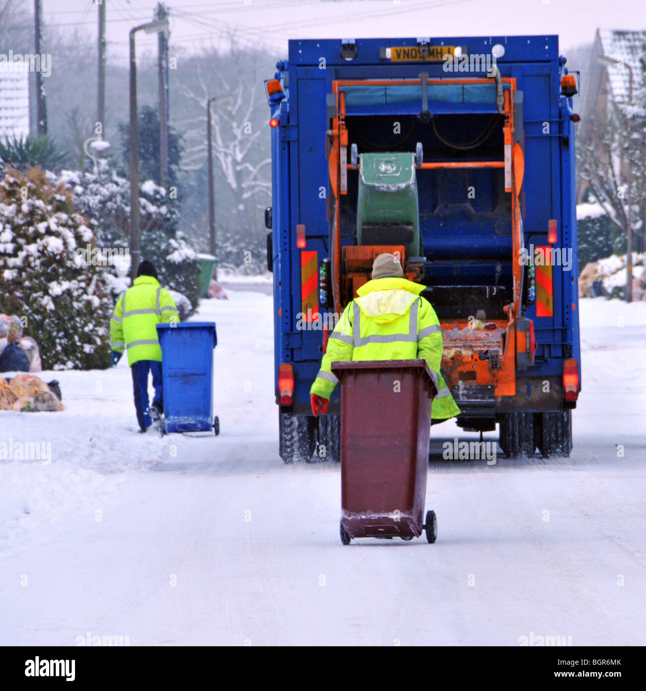 Rückansicht Council Müllwagen LKW Binmen bei der Arbeit tragen gut sichtbare Winterjacken Eisschnee bedeckt unbehandelte Wohnstraße Essex England Stockfoto