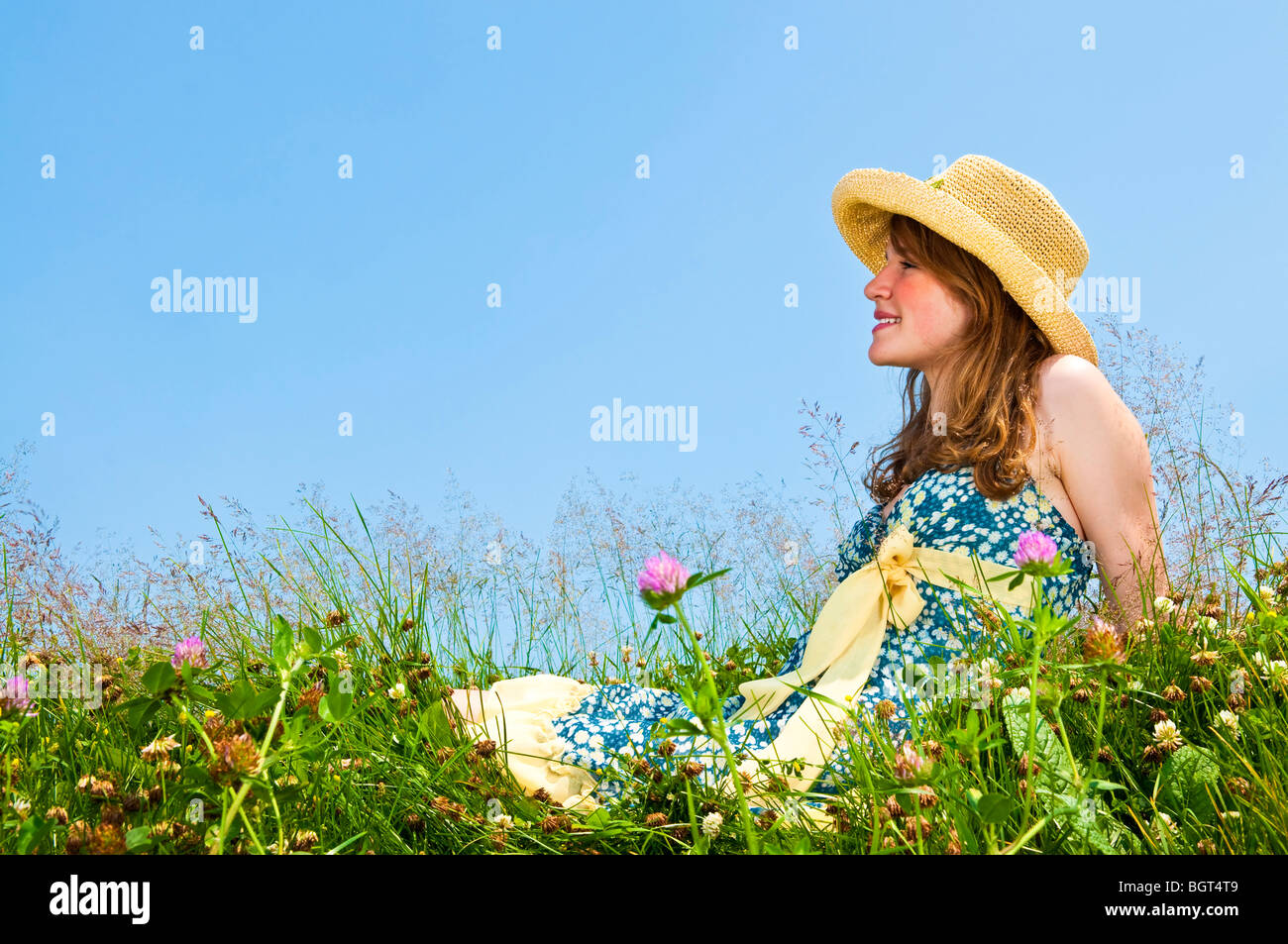 Junge Teenager-Mädchen sitzen auf Sommerwiese im Strohhut Stockfoto