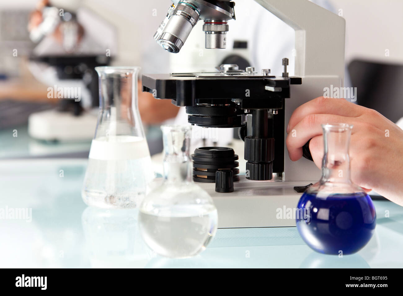 Eine medizinische oder wissenschaftliche Forscher mit Hilfe eines Mikroskops und Fläschchen Flüssigkeit in einem Forschungslabor. Stockfoto