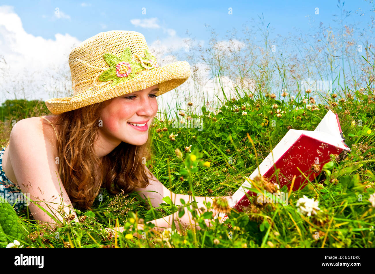 Porträt von Teenager-Mädchen-Lesebuch in Sommerwiese mit Strohhut Stockfoto