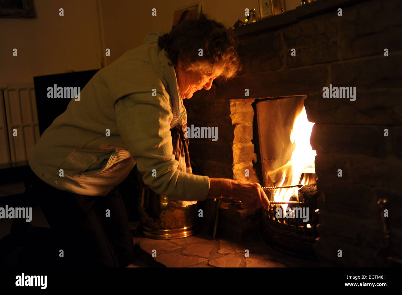 Die Rentnerin zündet ein offenes Feuer an, um sich in ihrem Haus warm zu halten, während sie versucht, die Strom- und Gasrechnungen in Großbritannien zu sparen Stockfoto