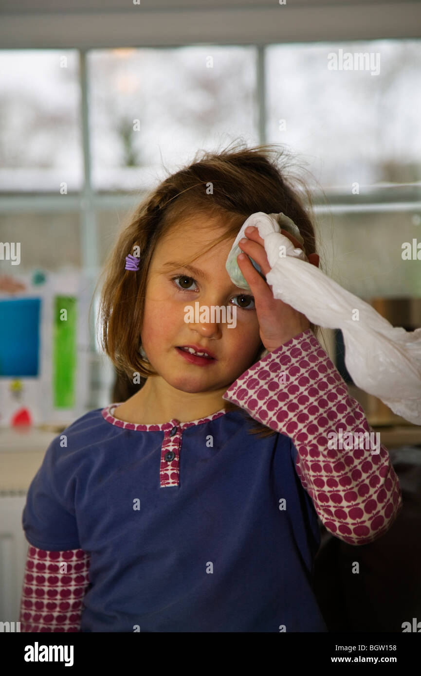 Kleines Mädchen mit Beule am Kopf einige gefrorenen Erbsen festhalten Stockfoto