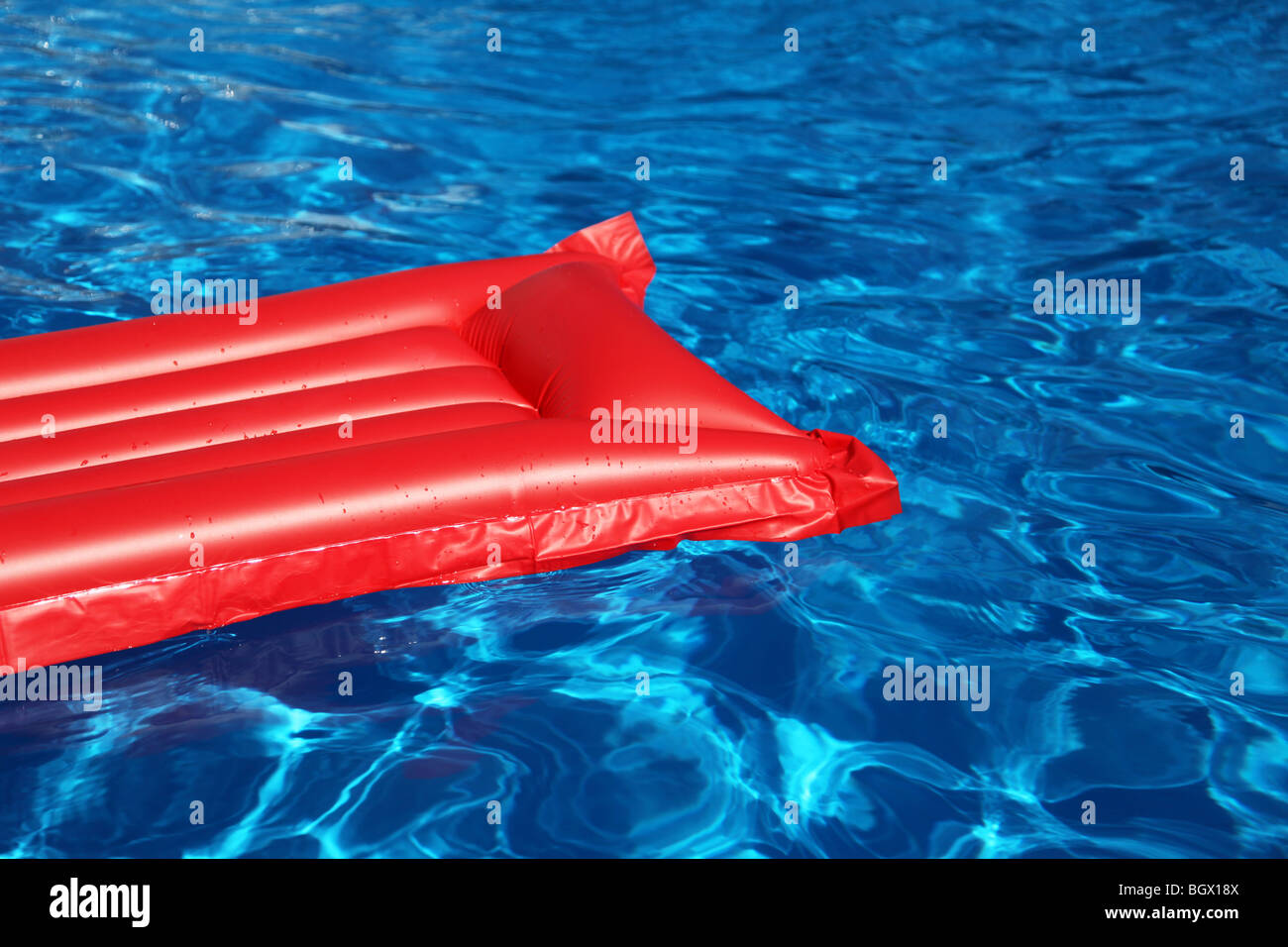 Eine aufblasbare rote Luftmatratze in einem glänzenden blauen Swimmingpool schwimmen. Stockfoto