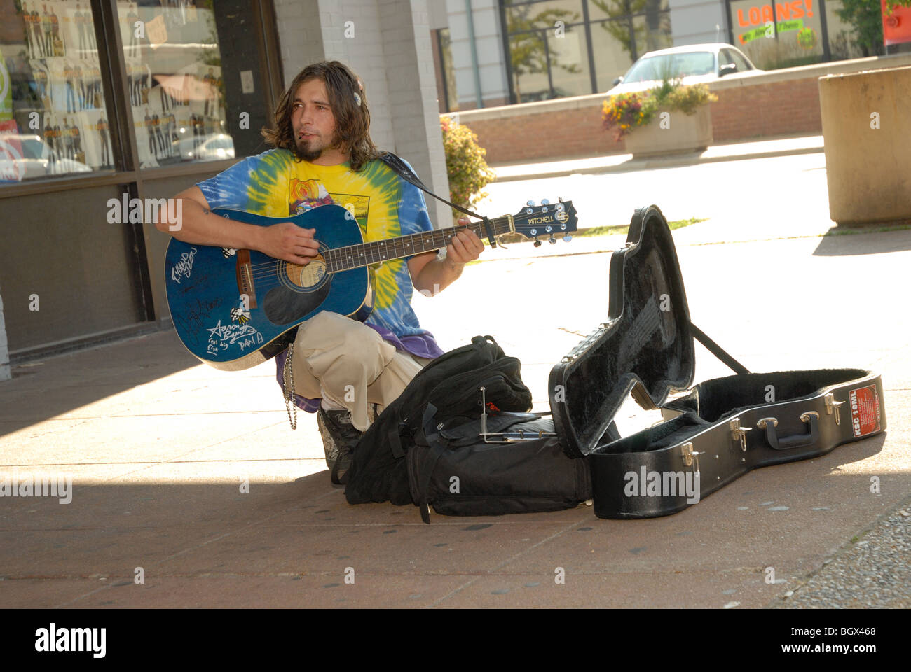 Das Foto zeigt ein Straßenkünstler Gitarre spielen und singen außerhalb auf einer öffentlichen Straße Ecke, Gitarrenkoffer offen für Beiträge. Stockfoto