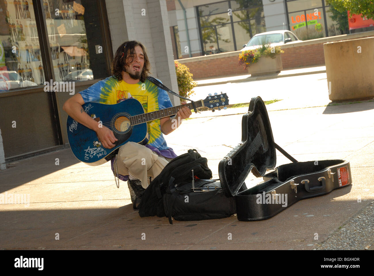 Das Foto zeigt ein Straßenkünstler Gitarre spielen und singen außerhalb auf einer öffentlichen Straße Ecke, Gitarrenkoffer offen für Beiträge. Stockfoto
