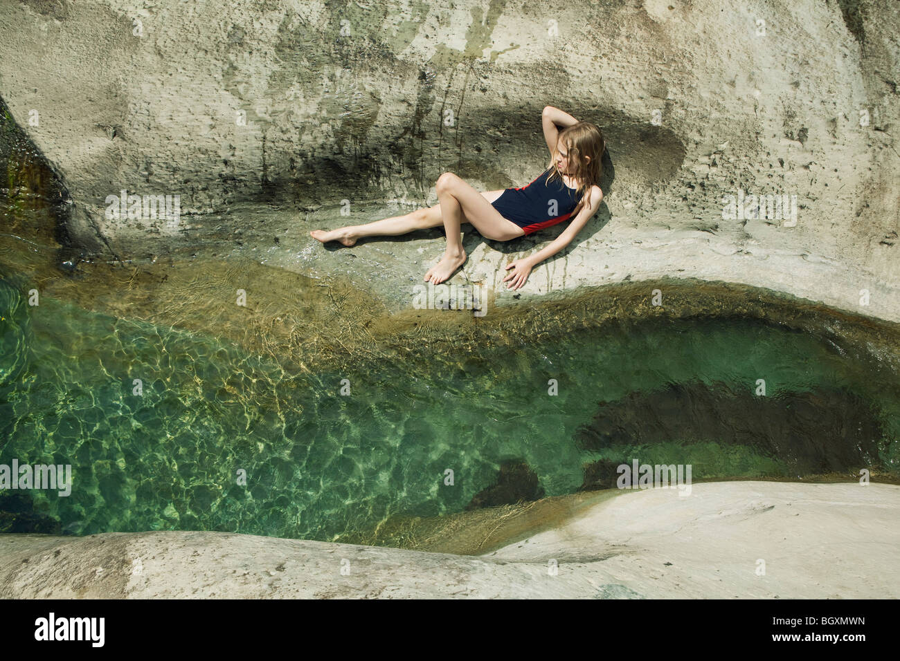 Mädchen liegend auf Felsen neben Bach Stockfoto