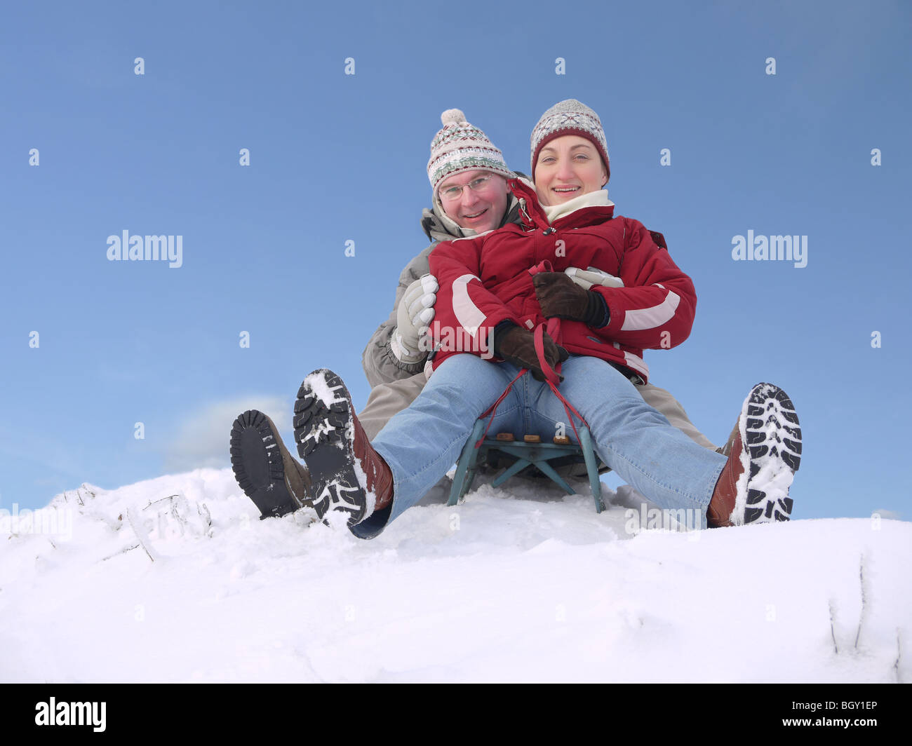 Junges Paar geht den Hügel hinunter auf Schlitten im winter Stockfoto
