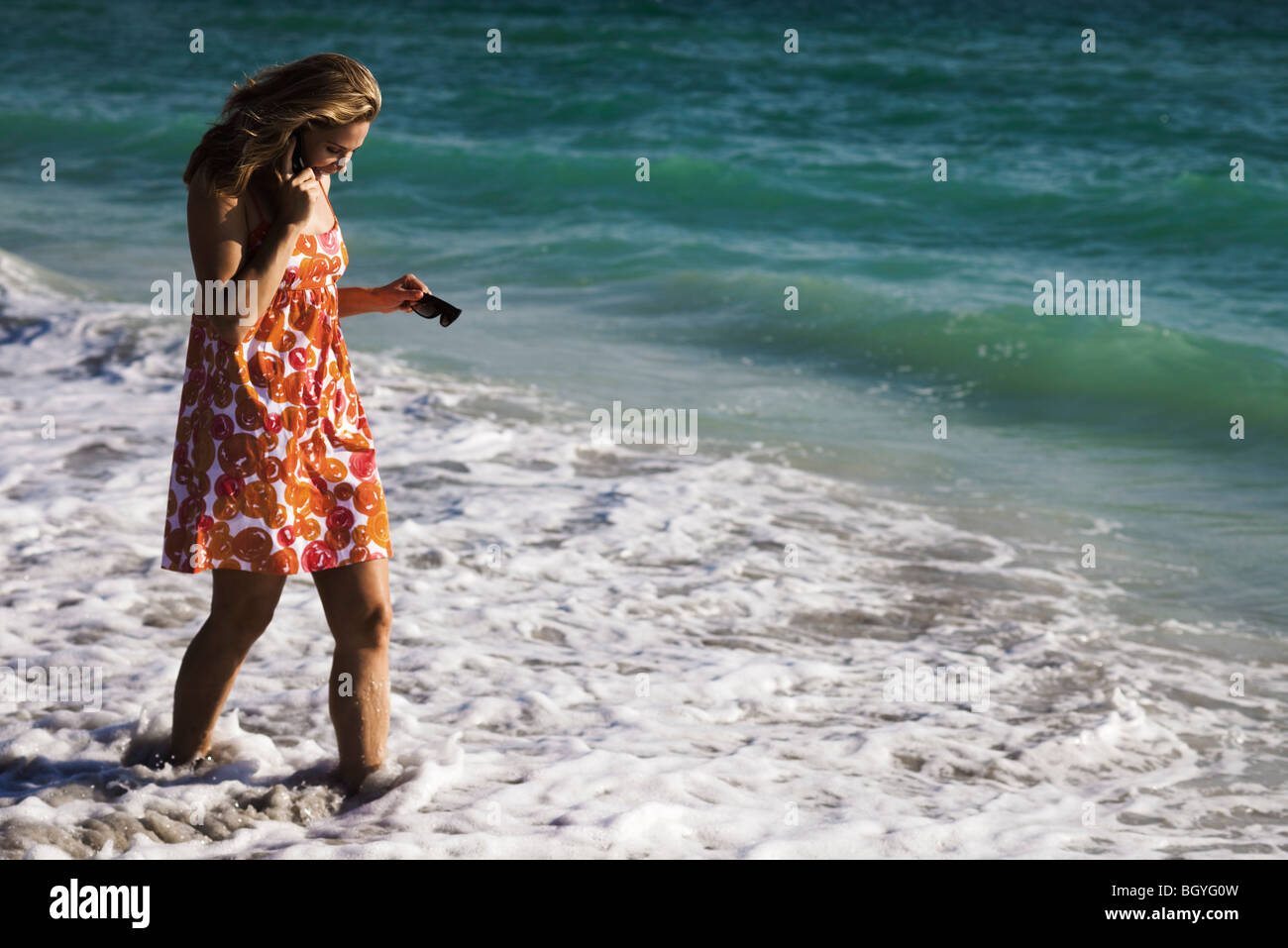 Frau in Brandung am Strand, zu Fuß am Handy Stockfoto