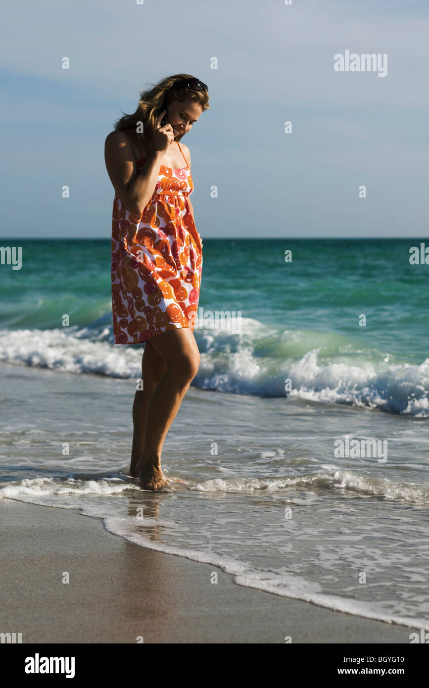 Frau in Brandung am Strand, zu Fuß am Handy Stockfoto