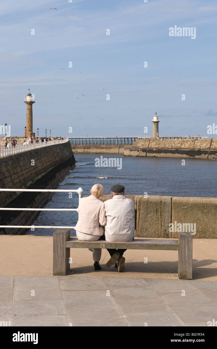 Zwei Menschen sitzen auf einer Bank mit Blick über dem Eingang zur Whitby Hafen. Stockfoto