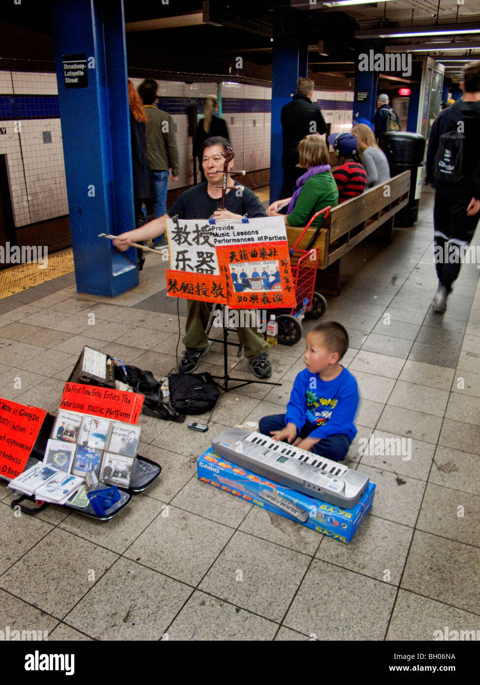 Eine asiatische Musiker wird von seinem kleinen Sohn begleitet, wie sie ein Duett für Spenden an einer u-Bahnstation in New York City spielen. Stockfoto