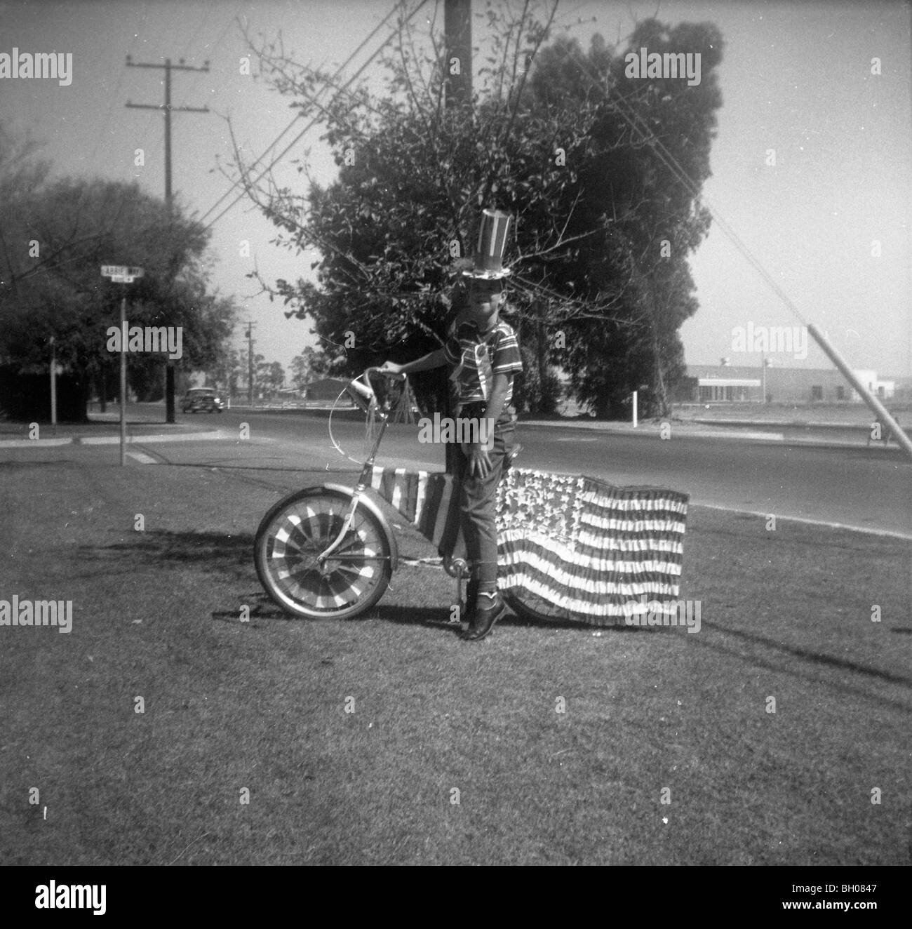 Ein Junge gekleidet wie Uncle Sam posiert für ein Foto mit seinem Fahrrad dekoriert mit den Sternen und Streifen und eine amerikanische Flagge. Stockfoto