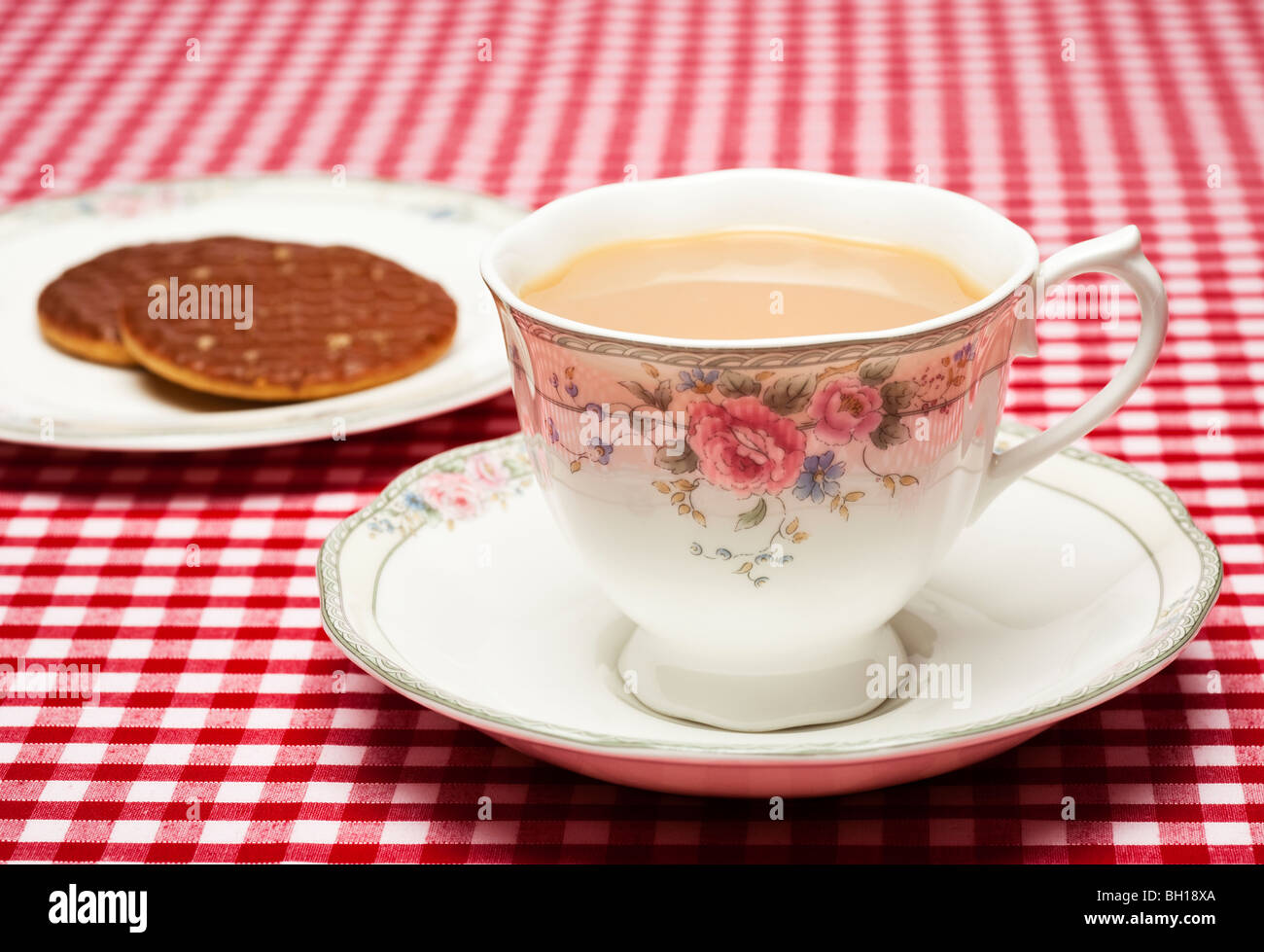 In einer feinen Bone China Tasse Tee dekoriert, Tasse und Untertasse mit einem Teller Kekse auf einem roten aufgegebenes Tischdecke Stockfoto