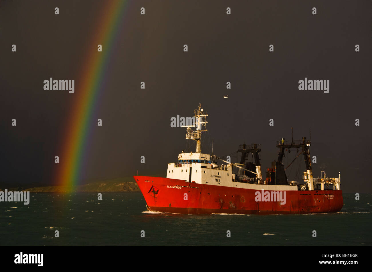 Ein Fischereifahrzeug fährt vom Hafen mit einer stürmischen Himmel und Regenbogen im Hintergrund. Stockfoto