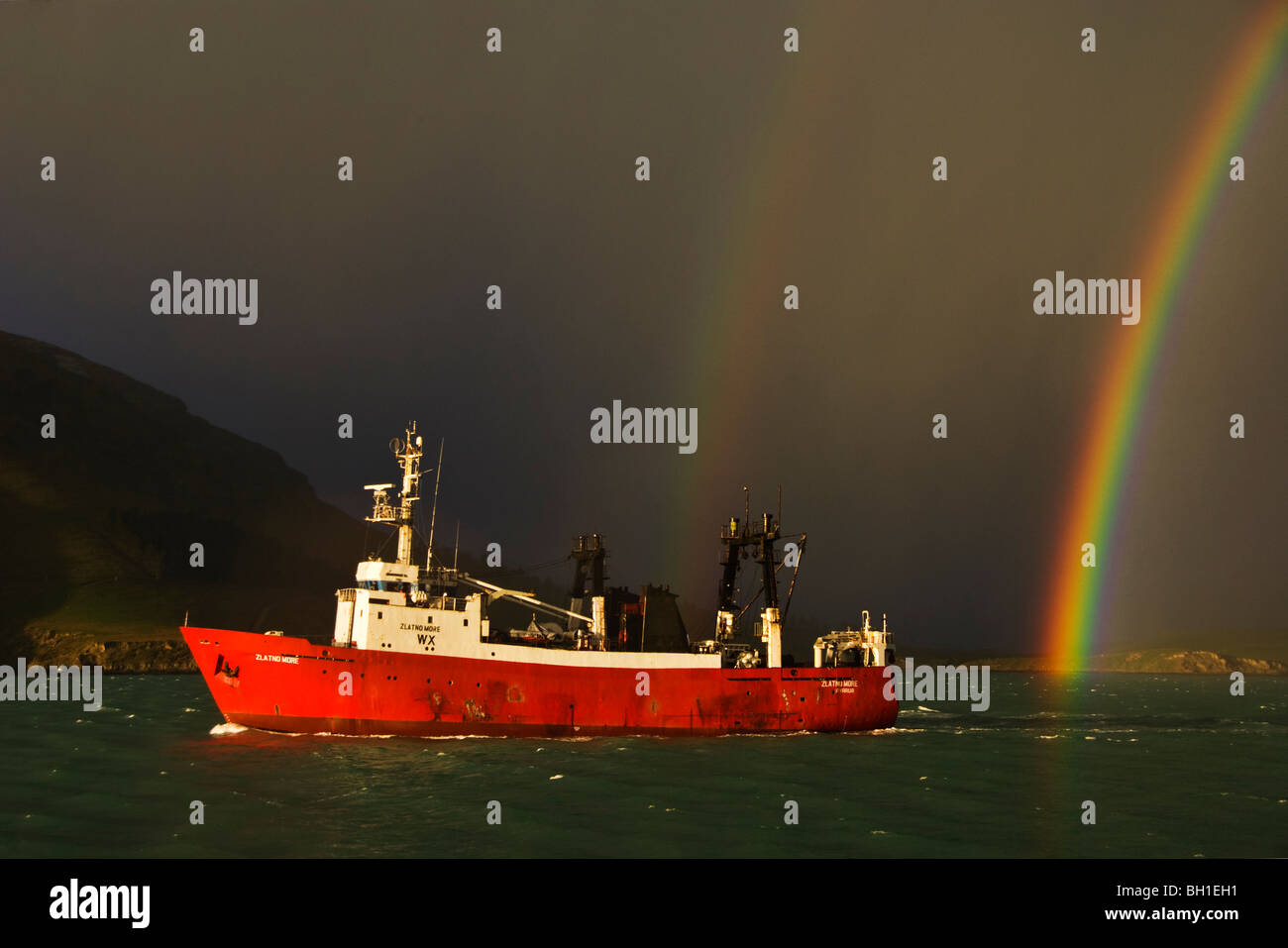 Ein Fischereifahrzeug fährt vom Hafen mit einer stürmischen Himmel und Regenbogen im Hintergrund. Stockfoto