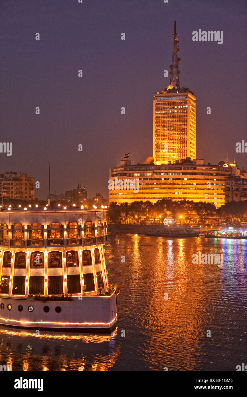 Beleuchtetes Schiff auf dem Nil vor dem Hochhaus des ägyptischen Fernsehen Center, Kairo, Ägypten, Afrika Stockfoto
