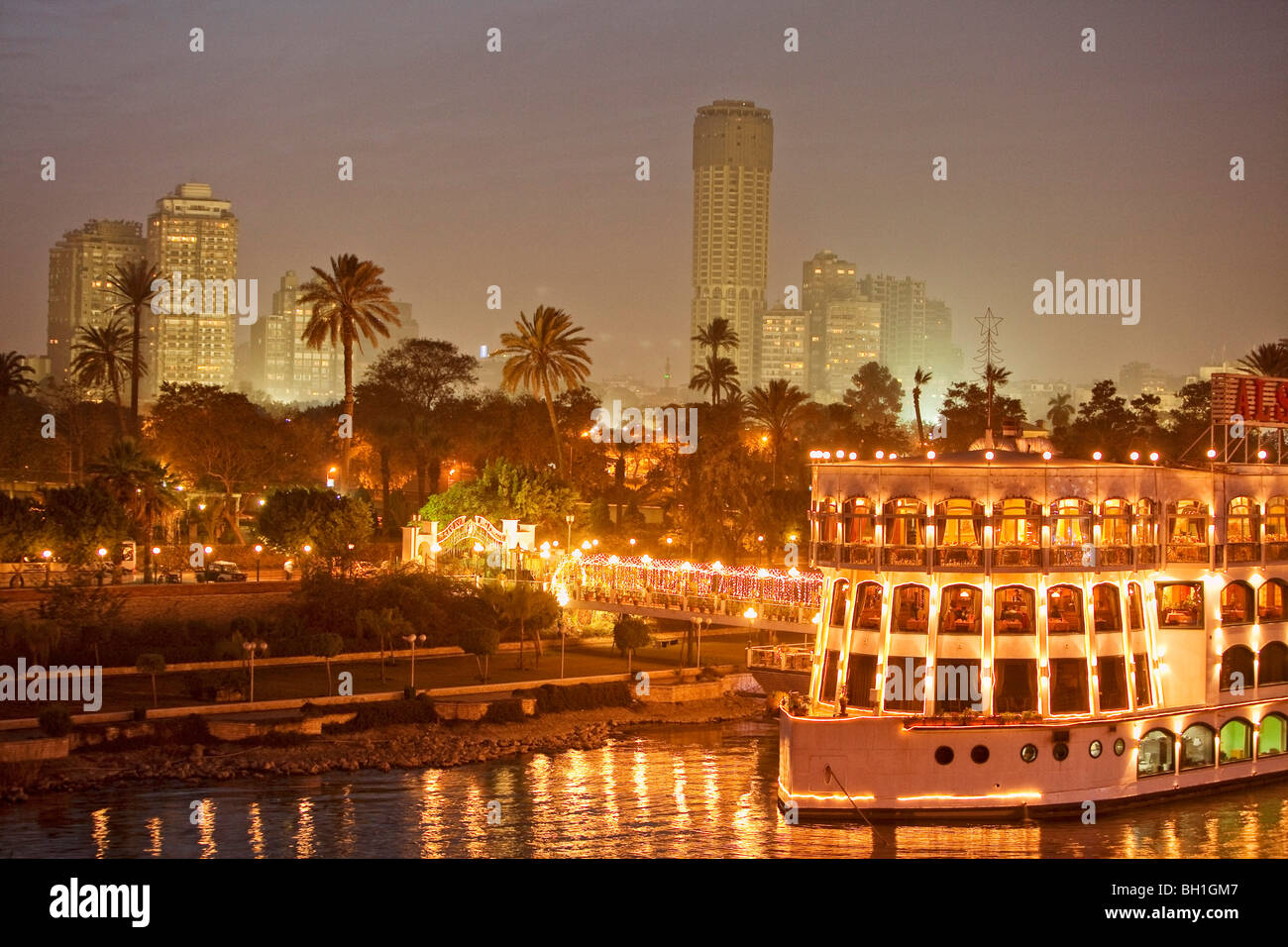 Beleuchtetes Schiff auf dem Nil vor Palmen und hohen Aufstieg Gebäude, Kairo, Ägypten, Afrika Stockfoto