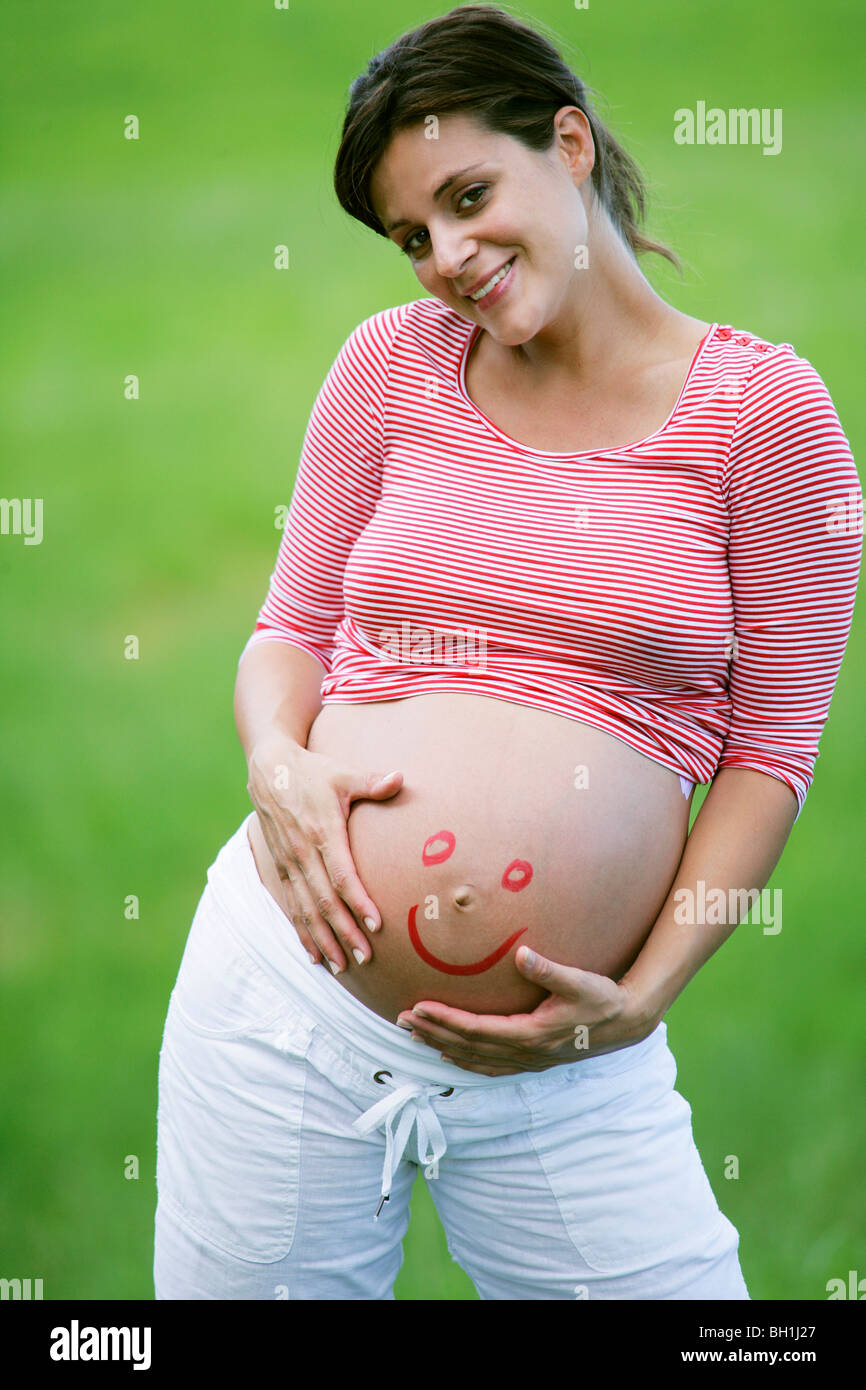 Schwangere Frau mit Smiley-Gesicht auf Bauch Stockfoto