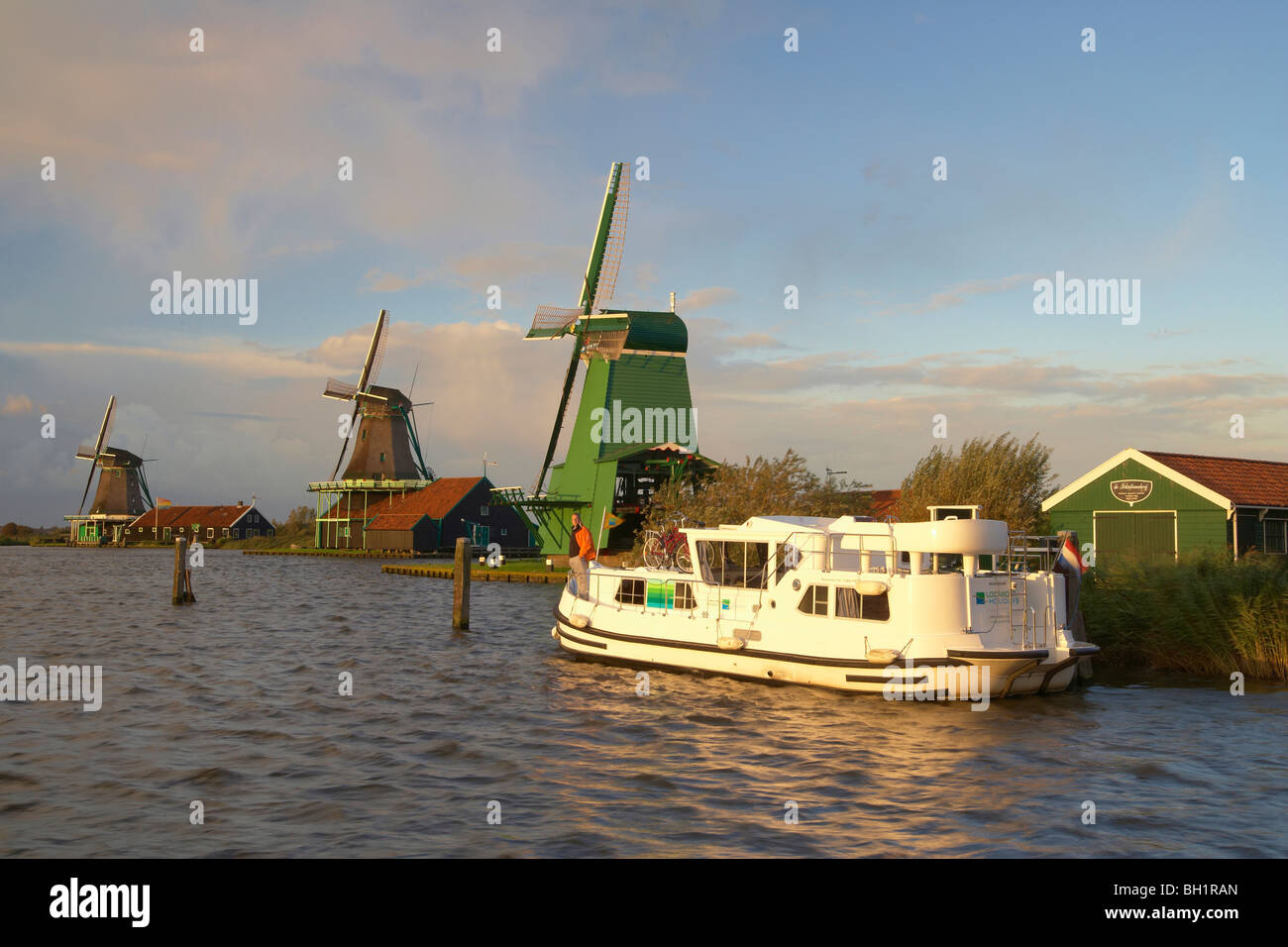 Ein Boot und Windmühlen im Licht der untergehenden Sonne, Freilichtmuseum Zaanseschans am Fluss Zaan, Niederlande, Europa Stockfoto