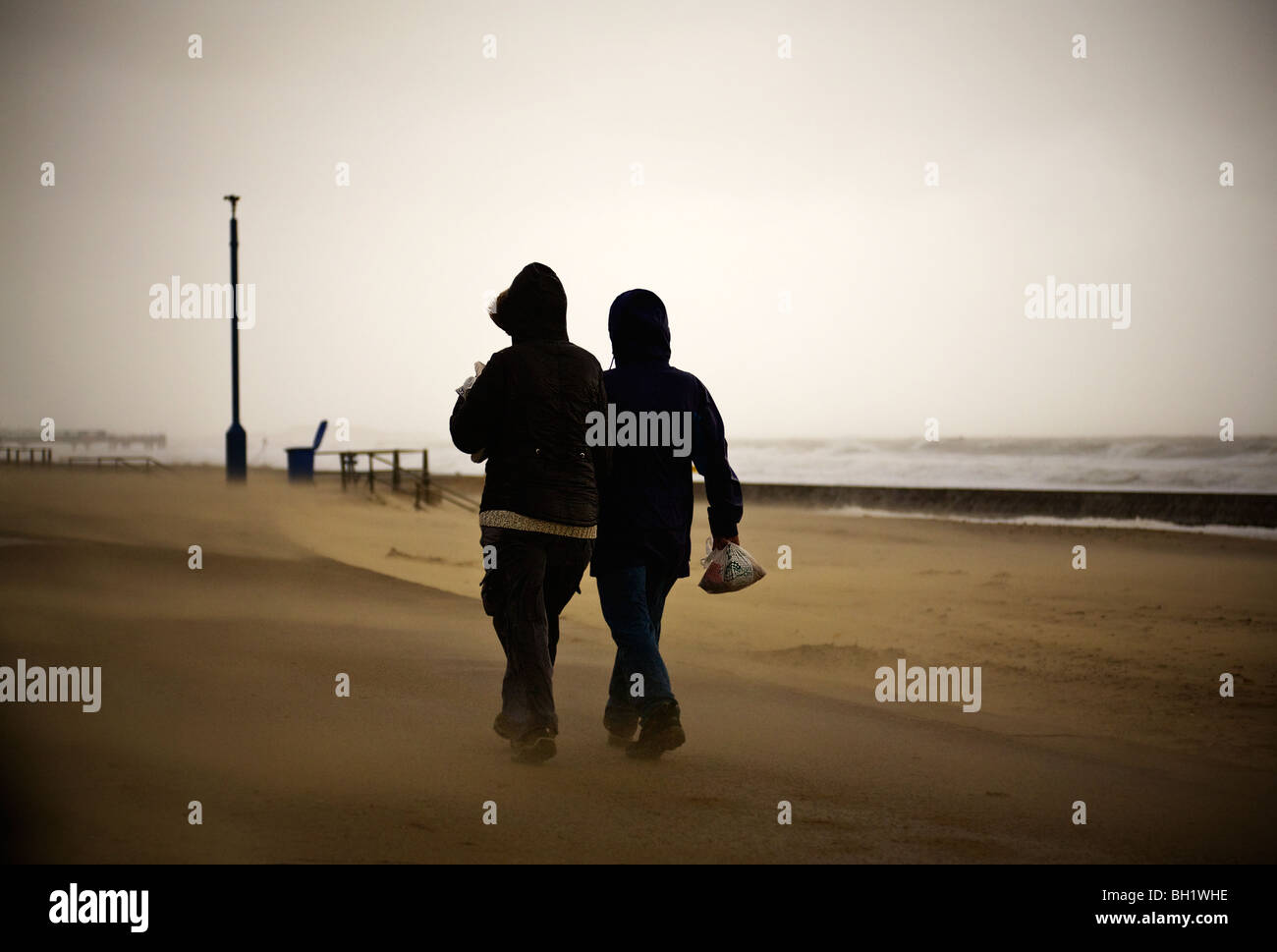 Menschen in extremen Wetterbedingungen. Sand ist am Strand und entlang der Strandpromenade von starkem Wind geblasen. Bournemouth. Dorset. VEREINIGTES KÖNIGREICH. Winter. Stockfoto