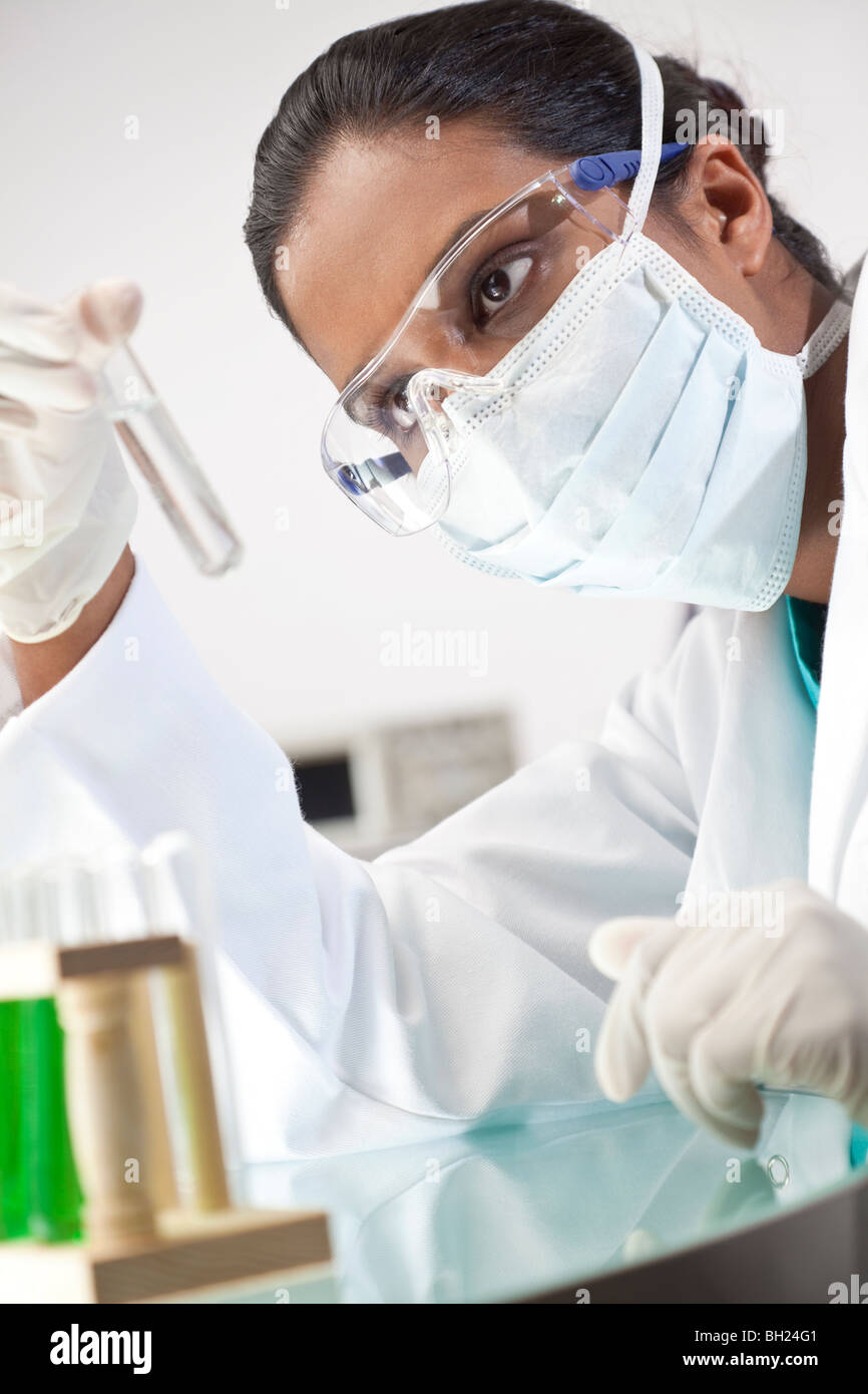 Weibliche asiatische medizinische oder wissenschaftliche Forscher oder Arzt ein Reagenzglas klare Lösung oder Flüssigkeit in einem Labor zu betrachten. Stockfoto