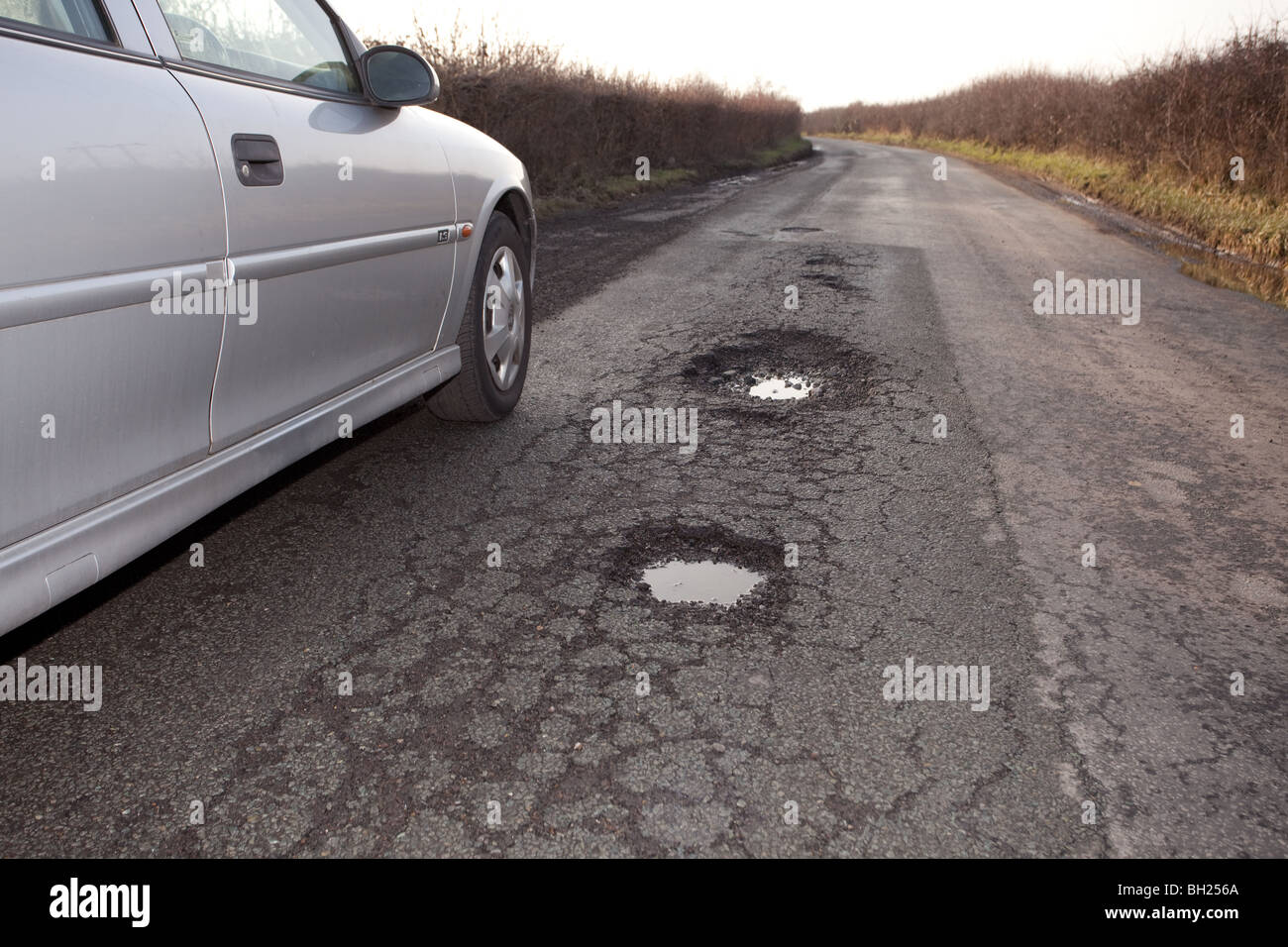 Schlaglöcher in einen Feldweg mit dem Auto neben ihnen ein Gefühl von Größe und Lage auf der Straße geparkt. Stockfoto