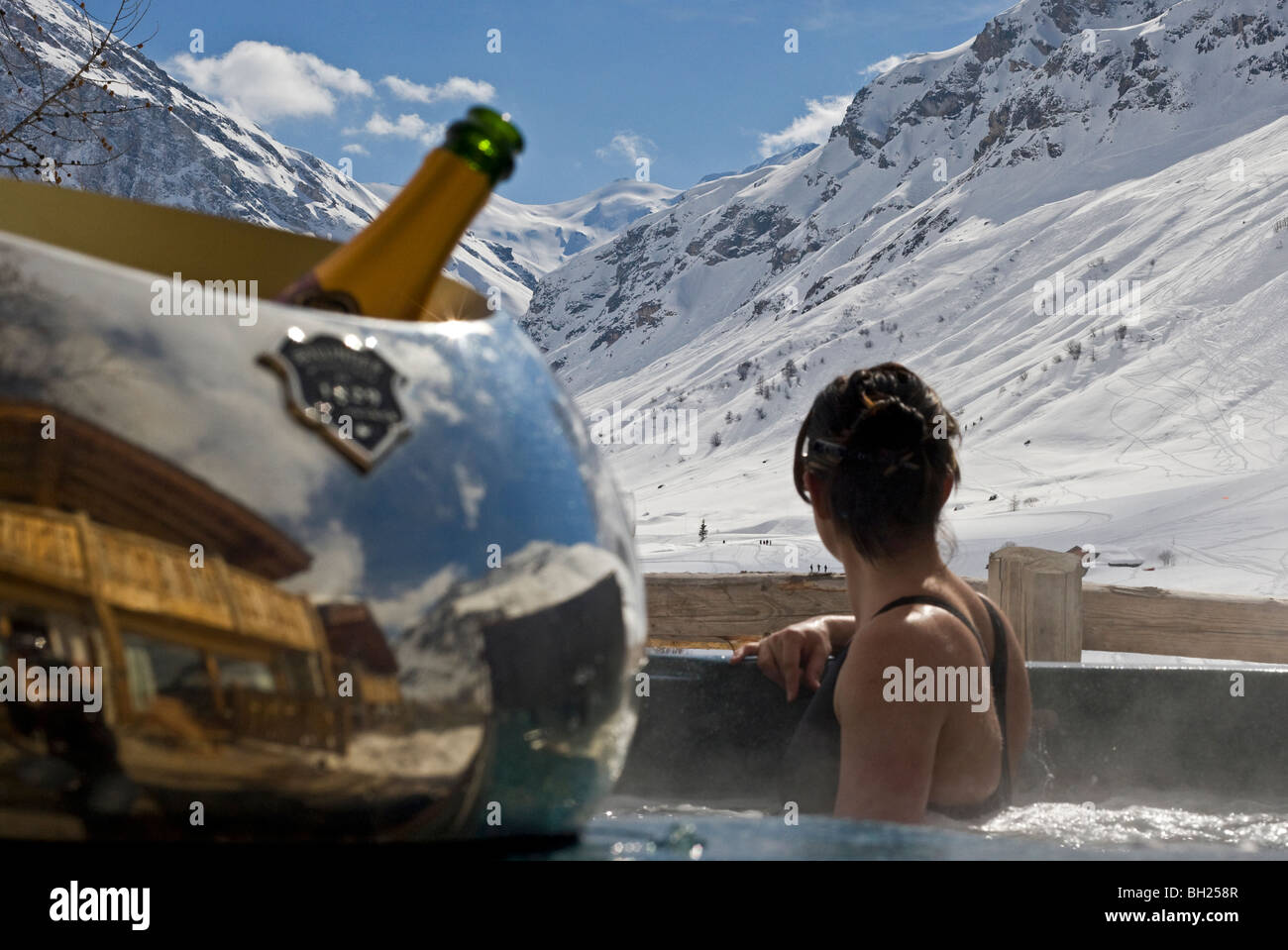 Frau sitzt in einem Whirlpool mit Blick auf Luxus Bergblick mit einer Flasche Champagner in Stockfoto