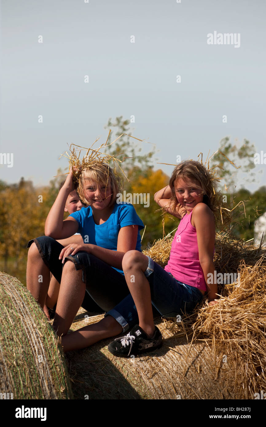 Zwei Mädchen (12 und 10) Holding Staw sitzen als wären es Haare, auf Ballen; Redvers, Saskatchewan, Kanada Stockfoto