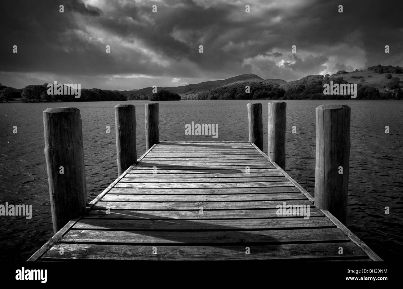 Monotone Bild von einer Anlegestelle in Coniston Water im Lake District mit dramatische Wolken und sonnenbeschienenen Hügeln. Stockfoto
