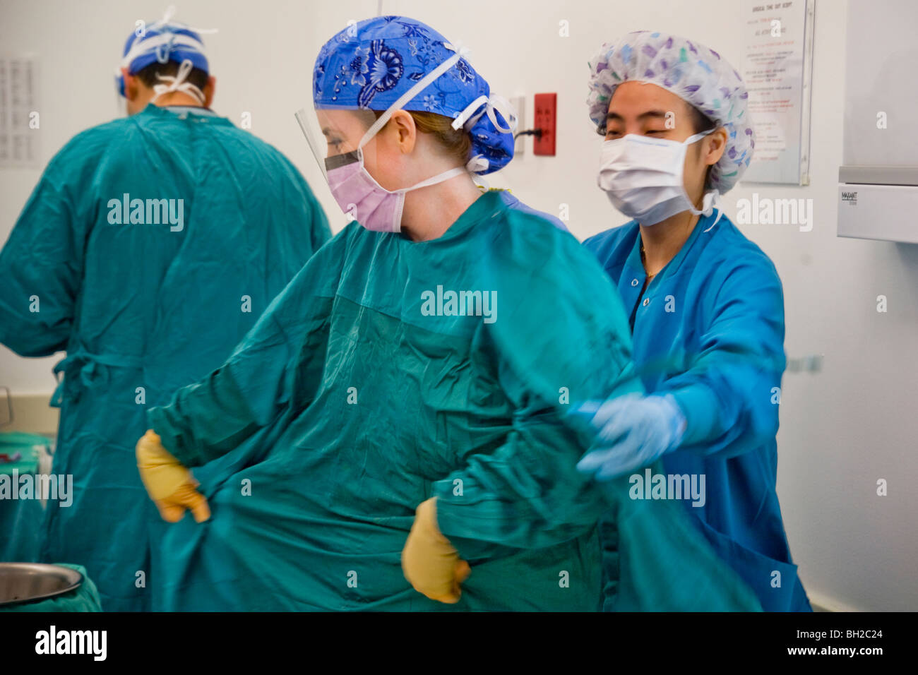 Frau Chirurg wird aus ihrer sterilen Robe von ihrem zirkulierenden Krankenschwester unterstützt, nach dem Ausführen eines Vorgangs. Stockfoto